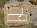 Widok z lotu ptaka na plac budowy. Widać fundamenty domu, piasek, drewno i wykopy pod studnie fundamentowe.