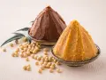 Dwie góry pasty miso, ciemna i jasna, obok ziaren soi i liści. Poznaj składniki do przygotowania tej aromatycznej pasty miso.