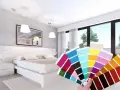 Una mano tiene un campionario di colori davanti a una moderna camera da letto bicolore, con pareti grigie e bianche e un letto bianco.