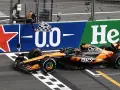 El coche de McLaren cruza la meta en el **Gran Premio Países Bajos**. El piloto celebra la victoria ondeando la bandera a cuadros.