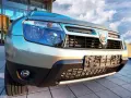 Złoty Dacia Duster 1.6 benzyna z chromowanym grillem i niebieskimi reflektorami, gotowy na przygodę pod błękitnym niebem.