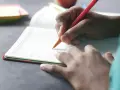 Dłoń pisze w zeszycie, co to dysgrafia? Trudności z pisaniem mogą dotyczyć każdego.