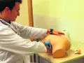 Mężczyzna w białym fartuchu ćwiczy samodzielne badanie prostaty na fantomie.