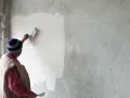 Un artisan applique un enduit chaux sable intérieur sur un mur avec une truelle. La texture naturelle du mortier est visible.