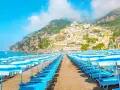 Rzędy leżaków i parasoli na plaży w Positano, Włochy. W tle widać malownicze miasteczko na zboczu góry i błękitne morze.
