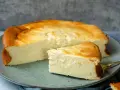 Ein saftiger Quarkkuchen ohne Boden, goldbraun gebacken, liegt auf einem Teller. Ein Stück ist bereits angeschnitten und zeigt die cremige Konsistenz.
