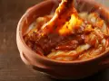 Cocochas de bacalao cubiertas con una salsa roja y burbujeante en una cazuela de barro.