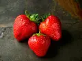 Trzy soczyste truskawki na ciemnym tle. Zastanawiasz się, ile kcal ma truskawka? To pyszna i niskokaloryczna przekąska.