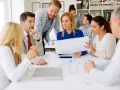A diverse group of professionals discusses documents, possibly during board of directors recruitment or a strategic meeting.