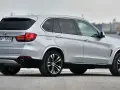 Srebrny BMW X5 z polskimi tablicami rejestracyjnymi stoi na betonowej nawierzchni, w tle widać port.