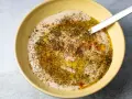Cremiger Hummus Aufstrich in gelber Schüssel, beträufelt mit Olivenöl und bestreut mit Kräutern und Paprika.