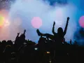 Tłum na jednym z największych festiwali muzycznych na świecie. Kobieta na rękach, ręce w górze, światła sceny.