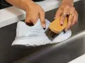 Mani che puliscono una scarpa da ginnastica bianca con una spazzola, mostrando come lavare le tn bianche per farle tornare come nuove.