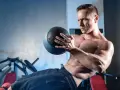 Un homme transpire en faisant un exercice oblique avec un ballon de médecine dans une salle de sport.