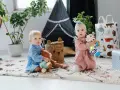 Dwoje dzieci bawi się na dywanie. Jedno trzyma misia, drugie kolorową zebrę. Idealne zabawki, co kładziemy dziecku na roczek.