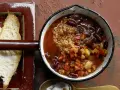 Herzhaftes Chili sin Carne mit Kidneybohnen, Bulgur und Gemüse in einem Topf, daneben geröstetes Brot.