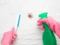 Mains gantées de rose utilisant un spray et une brosse pour enlever une tache de sang déjà lavée sur un matelas blanc.