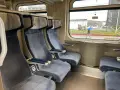Wygodne siedzenia w wagonie z przedziałami Intercity 2 klasa. Za oknem deszczowa pogoda i przechodzień z niebieskim parasolem.