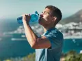 Un jeune homme boit dans une gourde bleue, se réhydratant après l'effort. L'eau, essentielle, contient des électrolytes pour le bon fonctionnement du corps.