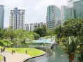 Park z rzeźbą wieloryba i basenem w stolicy Malezji, Kuala Lumpur, otoczony nowoczesnymi wieżowcami.