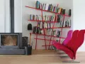 Camino acceso, attrezzi da camino, e moderne piccole librerie rosse piene di libri, con sedie colorate.