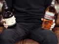 Mann hält Flaschen von Redbreast (irischer Whiskey) und Auchentoshan (schottischer Whiskey), um den Unterschied zu zeigen.
