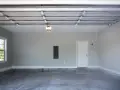 Pusta przestrzeń garażowa z oknem, drzwiami i skrzynką elektryczną. Zadbano o wentylację w garażu.