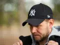 Mężczyzna w czarnej czapce z daszkiem z logo NY i szarej bluzie.