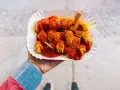Eine Hand hält eine Portion Currywurst mit original Currywurst Sauce, bestreut mit Currypulver. Ein Holzspieß steckt darin.