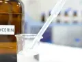 Braunglasflasche mit der Aufschrift "Glycerin". Ein Pipette tropft in ein Becherglas mit klarer Flüssigkeit, was die Glycerin verwendung in der Forschung zeigt.