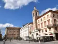 Piazza Tre Martiri a Rimini: un campanile con orologio domina la scena, tra palazzi storici e tavolini all'aperto. Ecco cosa vedere!
