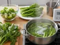 Préparation pour la cuisson d'épinards frais. Des légumes verts bouillent dans une casserole, d'autres attendent sur une assiette et une planche à découper.