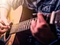 Ręce grające na gitarze akustycznej. Idealne dla tych, którzy zaczynają swoją przygodę z nauką gry na gitarze dla początkujących.
