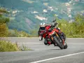 Un motociclista esperto piega in una curva stretta, con il ginocchio quasi a terra, affrontando un passo in montagna.