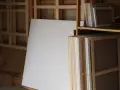 Un grand chevalet supporte une toile vierge. Des châssis entoilés, prêts à être peints, sont empilés, attendant l'inspiration.
