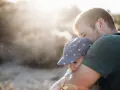 Ojciec mocno tuli dziecko w czapce z kwiatkami. To piękny moment, który pokazuje, jak ważny jest **asperger przytulanie** dla budowania więzi i poczucia bezpieczeństwa.