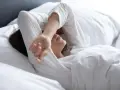 Kobieta w białej pościeli, z ręką na czole, zmaga się z bezsennością w ciąży.