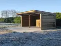 Abri pour chevaux d'occasion en bois, avec toit métallique, sur un sol gelé. Parfait pour protéger vos équidés du froid.