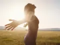 Frau mit ausgebreiteten Armen im Sonnenlicht, ein Symbol für das Heilen von Hypochondrie und das Finden von innerem Frieden.