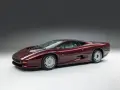 Bordowy Jaguar XJ220, ikona motoryzacji lat 90., prezentuje swoje aerodynamiczne linie na tle szarego tła.