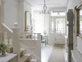 Jasny hol w stylu angielskim z białą klatką schodową, witrażowymi drzwiami i ozdobnym lustrem.