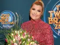 Małgorzata Szudarska Kuszewska z bukietem tulipanów na tle logo "Twoja twarz brzmi znajomo".