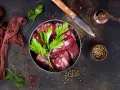 Świeża wątróbka w misce, gotowa do mrożenia. Obok nóż, przyprawy i gałązka pietruszki.