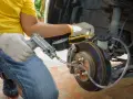 Mechanik w białych rękawiczkach wykonuje odpowietrzanie hamulców z ABS przy użyciu specjalnego narzędzia z manometrem.