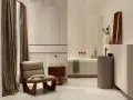 Elegancka łazienka z płytkami imitującymi trawertyn, wygodnym fotelem i wanną.