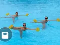 Trois femmes souriantes font un exercice aquagym dans une piscine, tenant des haltères flottants jaunes pour un entraînement tonique.
