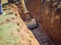Koparka pogłębia wykop pod garaż. Widać jaki głęboki fundament pod garaż powstaje.