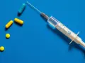Strzykawka z igłą i kilka tabletek, w tym kapsułki. Może to być przygotowanie do zastrzyku hormonalnego.