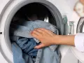 Dłoń wkłada jeansy do pralki. Dowiedz się, jak prać jeansy, by służyły latami.