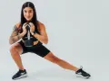 Donna con tatuaggi esegue affondo laterale con manubrio, dimostrando cos'è la palestra funzionale.